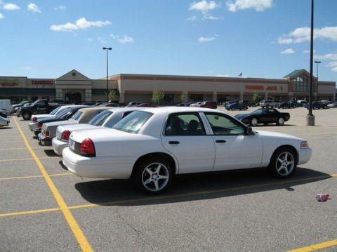 1988 Mercury Grand Marquis - White Ford Crown Victoria four-door sedan on five-spoke alloy wheels, parked at an angle across yellow-striped spaces in a strip-mall lot i…