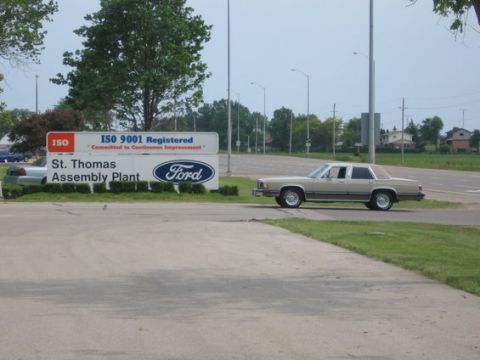 1988 Mercury Grand Marquis - A tan Mercury four-door sedan parked on the grass beside the entrance sign for Ford's St. Thomas Assembly Plant, which reads "ISO 9001 Regi…