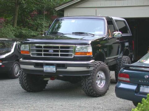 1996 Ford Bronco - A lifted 1996 Ford Bronco is parked in front of a garage, with another vehicle visible to its right.