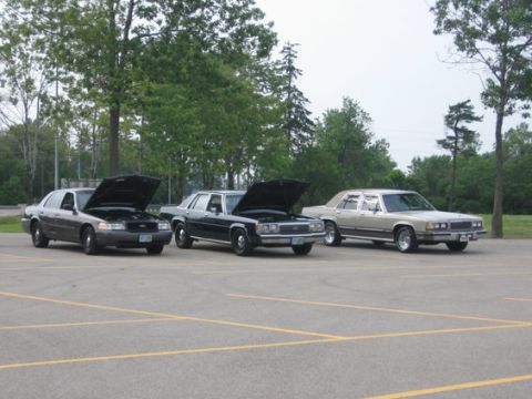 1988 Mercury Grand Marquis - Three sedans, including a 1988 Mercury Grand Marquis, are parked in a lot with their hoods open.