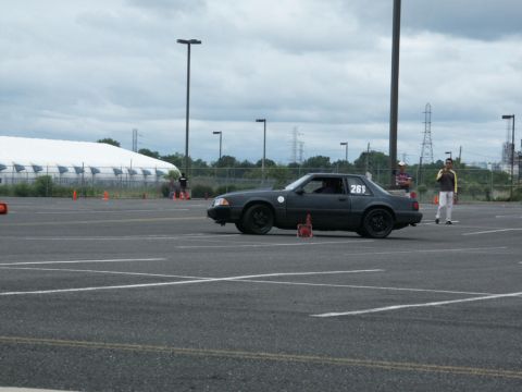 2001 Mercury Grand Marquis - A dark gray Ford Mustang is seen on an asphalt lot with orange cones and a large white tent in the background.