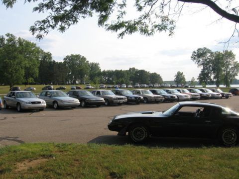 1988 Mercury Grand Marquis - A variety of cars are parked in a lot near a body of water on a cloudy day.