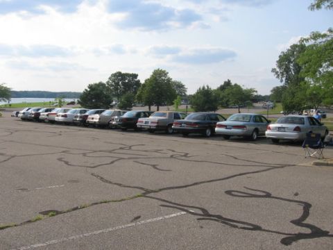 1988 Mercury Grand Marquis - A row of 1988 Mercury Grand Marquis sedans are parked in a lot near a body of water.