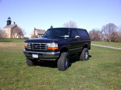 1996 Ford Bronco - A black 1996 Ford Bronco is parked on a grassy field with buildings and a lighthouse visible in the distance.