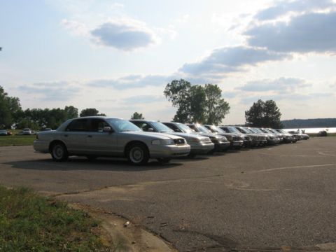 1988 Mercury Grand Marquis - Several sedans are parked in a line on a paved lot with a cloudy sky overhead.