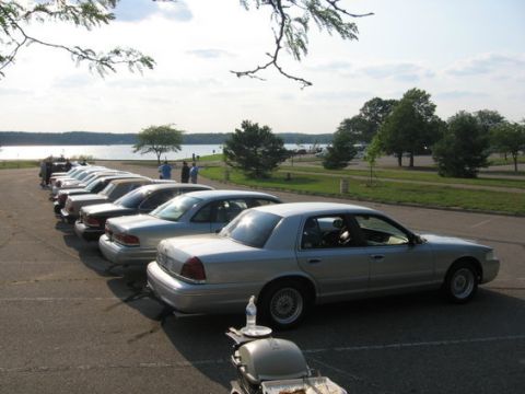 1988 Mercury Grand Marquis - A line of sedans, likely Ford Crown Victorias or Mercury Grand Marquis, parked near a body of water on a sunny day.