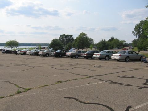 1988 Mercury Grand Marquis - Several sedans are parked in a lot near a body of water on a cloudy day.
