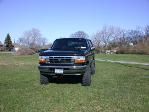 1996 Ford Bronco - A black Ford Bronco is shown from the front in a grassy field under a clear blue sky.