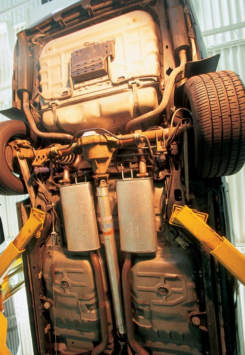 Underbody view of car fuel tank, dual mufflers and rear suspension on a lift