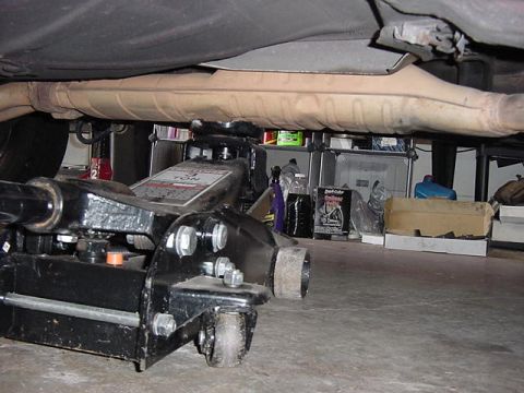 1984 BMW 3 Series - Underside view of a vehicle's exhaust system being supported by a 3-ton floor jack in a garage setting.