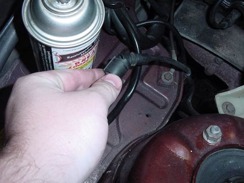 1984 BMW 3 Series - A hand disconnects a vacuum hose from a component in the engine bay, with a spray can nearby.
