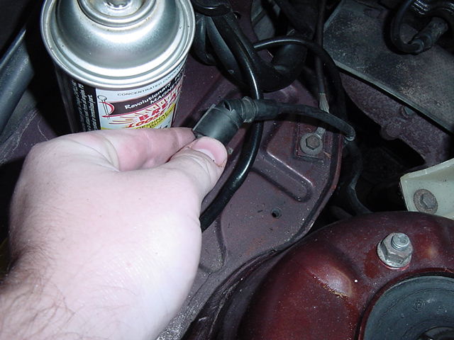 hand disconnecting a vacuum hose near a spray can in engine bay