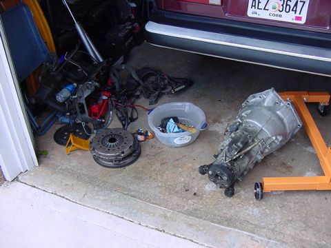 1984 BMW 3 Series - Car parts are laid out on the ground next to a car's rear end.