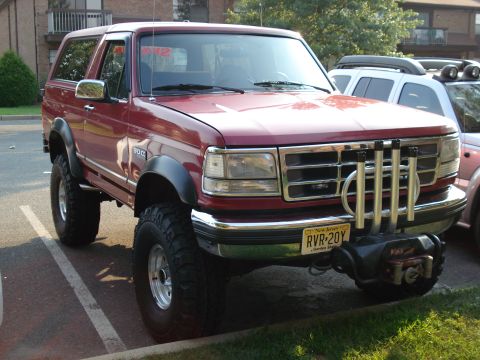 1994 Ford Bronco - Front three-quarter passenger-side view of a red lifted Ford Bronco in an apartment parking lot, with a Warn winch mounted below the chrome…