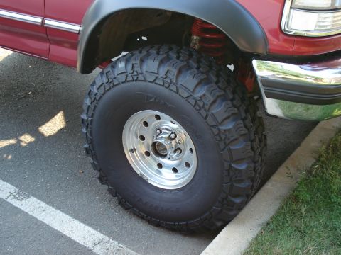 1994 Ford Bronco - Close-up of the front passenger wheel on a lifted red Ford truck, showing an aggressive Parnelli Jones Dirt Grip mud-terrain tire on a poli…
