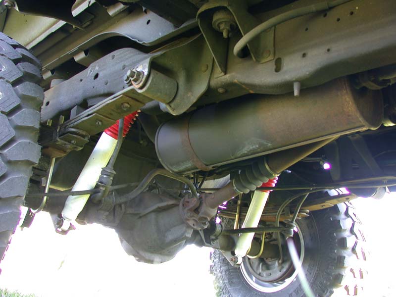 Underbody of lifted truck: leaf-sprung rear axle, white shocks with red boots, muffler