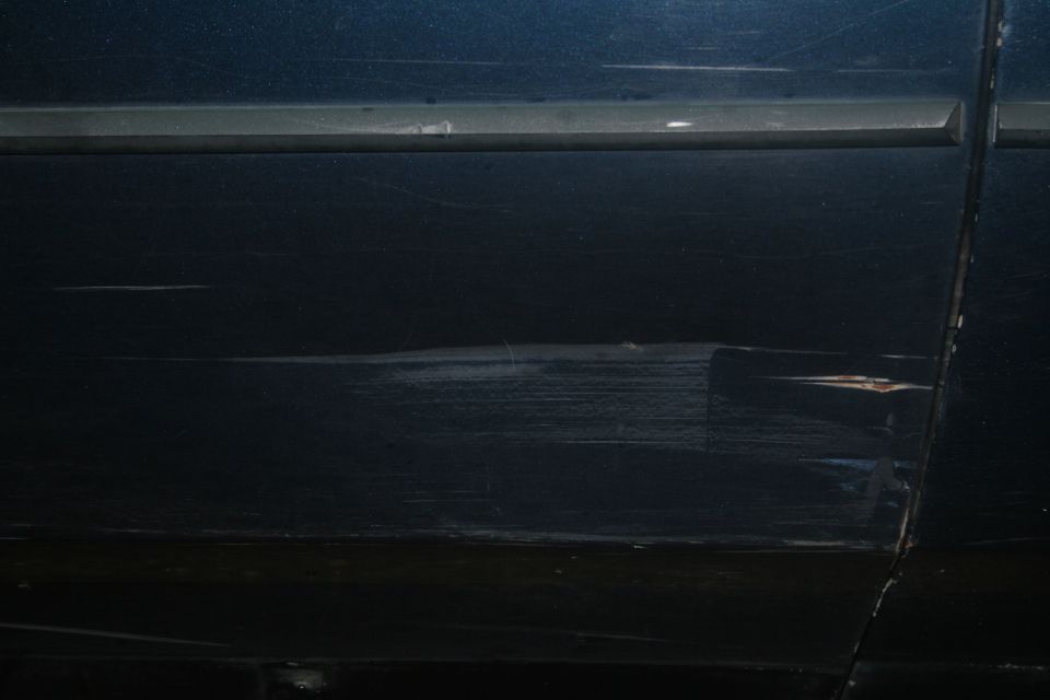 Close-up of deep scratches and damage on a dark-colored car door