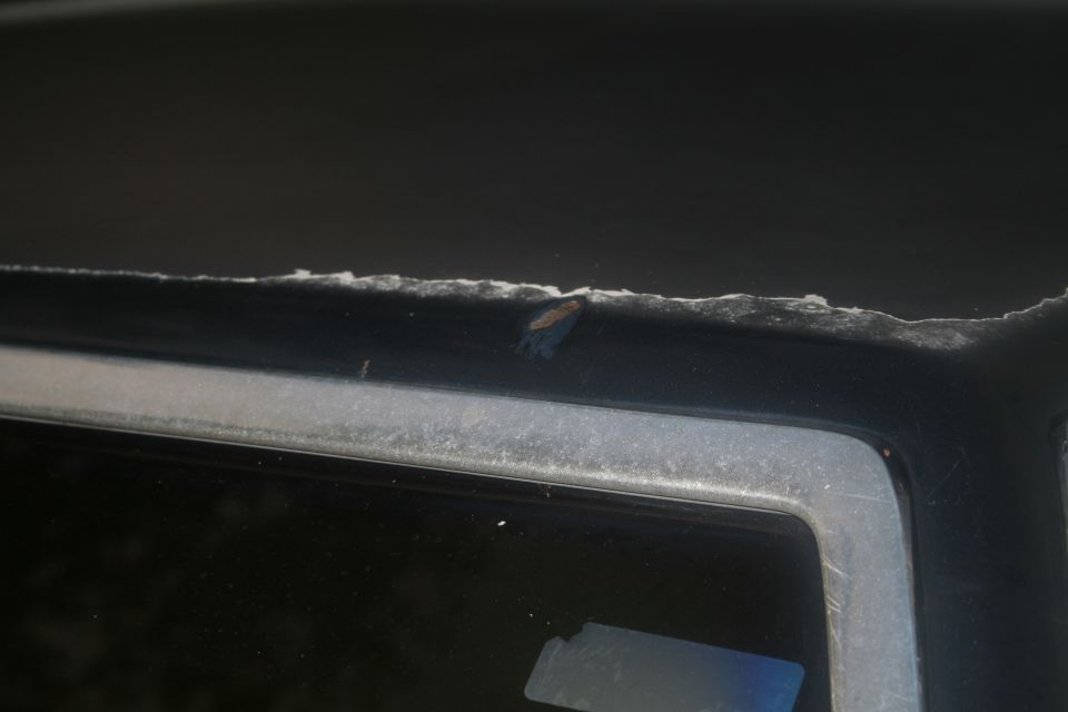 Close-up of cut sheetmetal edge above a car window with rust spot and filler dust