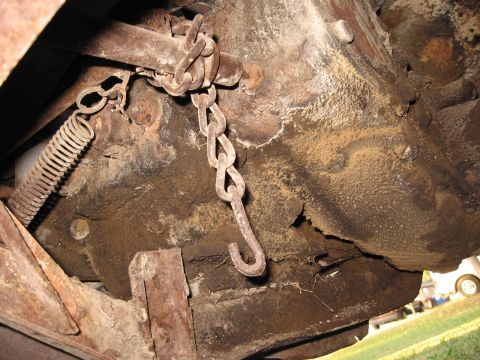 1983 Chevrolet Silverado 1500 - The underside of a vehicle displays a rusty chain and spring assembly, with visible wood supports.