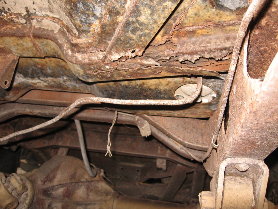 Undercarriage of a heavily rusted vehicle with exposed frame and fuel lines