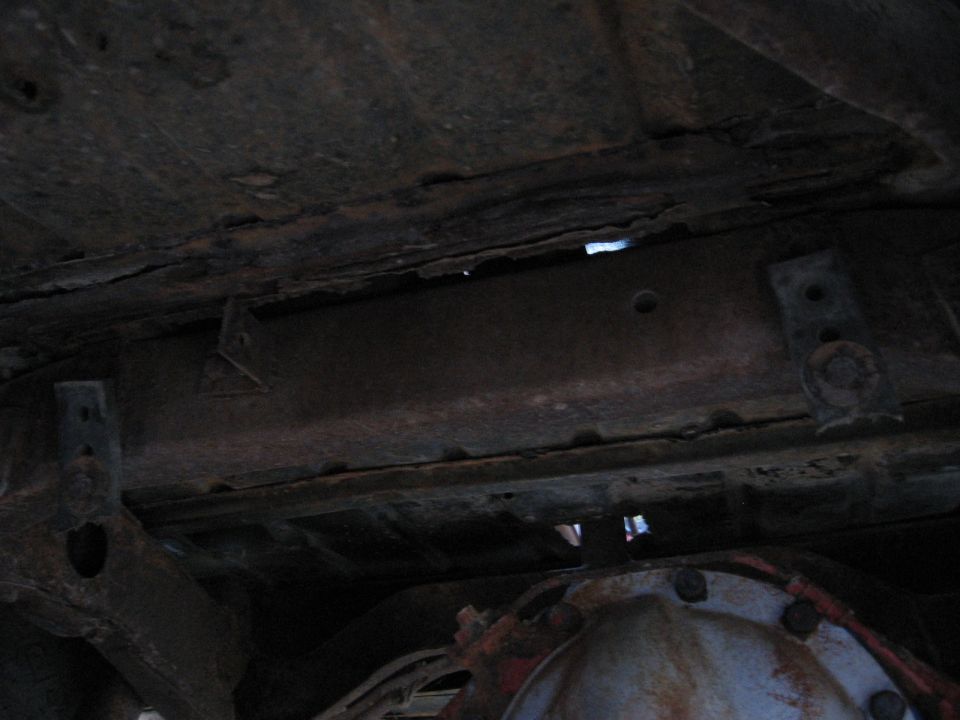 Underside view of a rusty vehicle frame with some suspension components visible. Supermotors.net logo in corner