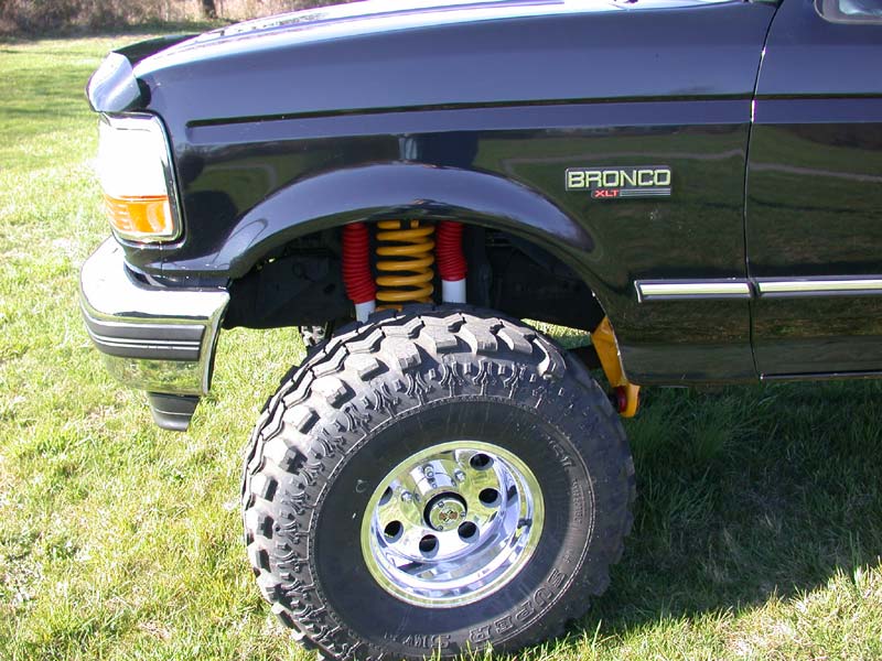 Black Ford Bronco XLT front corner with yellow coil spring, red shock and mud tires