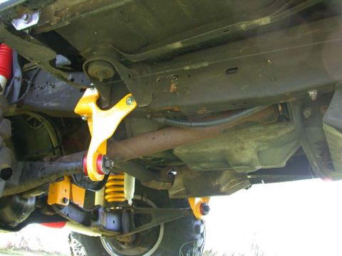 1996 Ford Bronco - Close-up of the underside of a vehicle, highlighting yellow aftermarket suspension parts and the exhaust system.