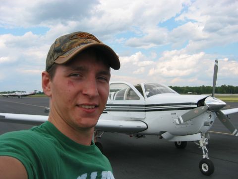 1989 Ford Bronco - A man in a camouflage hat takes a selfie with a small white airplane parked on the tarmac.