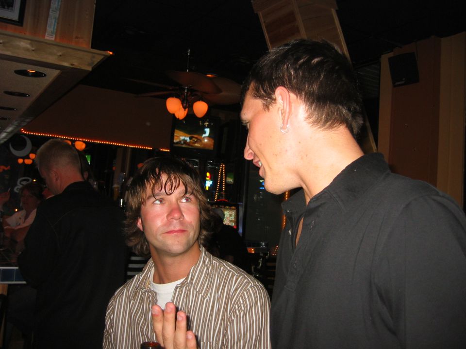 Two men talking inside a dimly lit bar