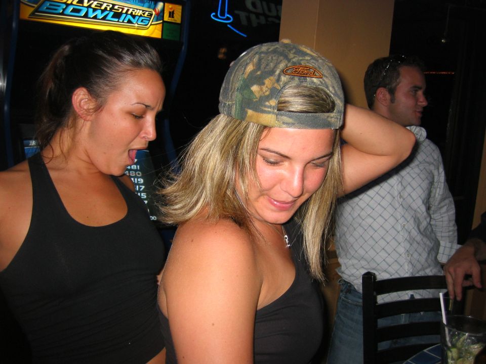 People at a bar, woman in backwards Ford camo cap, arcade game behind