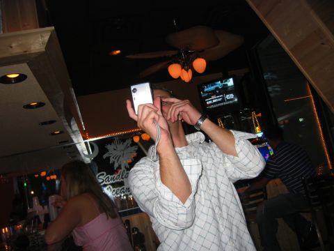 1989 Ford Bronco - A man is taking a photo with a digital camera in a bar or restaurant setting.
