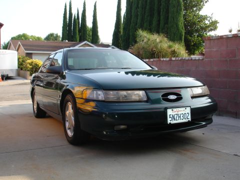 1995 Ford Taurus - A dark green sedan, identified as a 1995 Ford Taurus, is parked in a residential driveway.