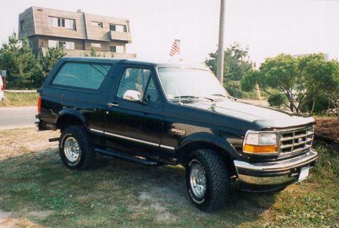 1996 Ford Bronco - This black 1996 Ford Bronco is seen from a 3/4 front angle, parked on a grassy area with a building in the background.