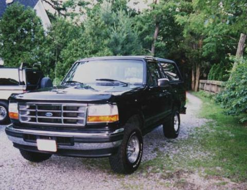 1996 Ford Bronco - A black Ford Bronco is parked on a gravel driveway next to trees and a wooden fence.