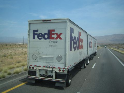 1990 Ford Bronco - white FedEx Freight semi pulling double trailers travels a desert interstate with distant mountains.