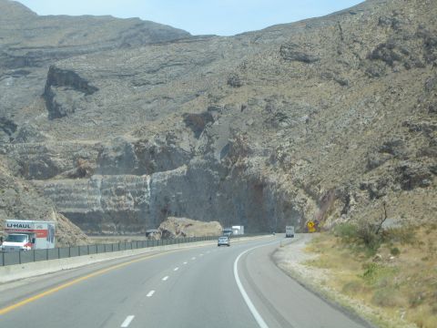 1990 Ford Bronco - highway curves below jagged rock cliffs in the desert as a U-Haul box truck passes on the left.