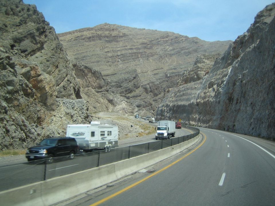 Highway through a desert canyon with an SUV towing a trailer and a semi