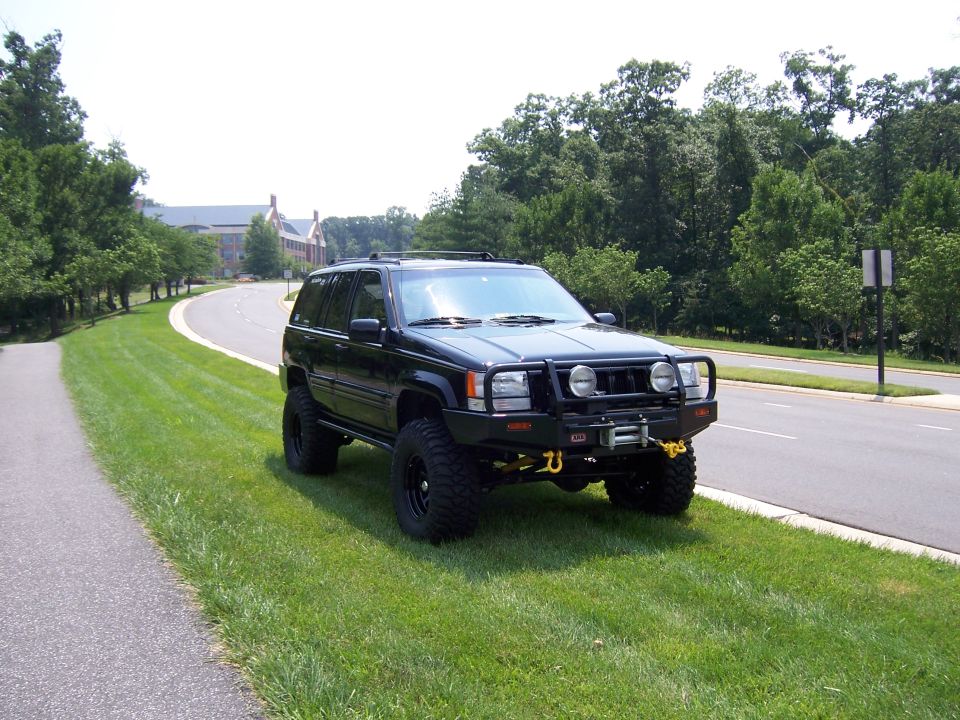 Lifted black Jeep Grand Cherokee ZJ with winch bumper and mud tires on grass
