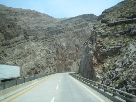 1990 Ford Bronco - two-lane highway winds between near-vertical layered rock walls as a white box truck approaches.