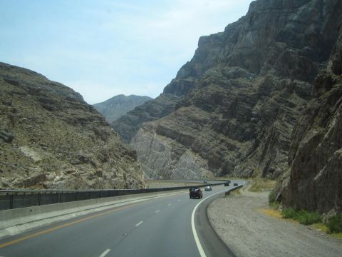 1990 Ford Bronco - highway sweeps through a steep folded-rock desert canyon with sparse traffic under hazy skies.
