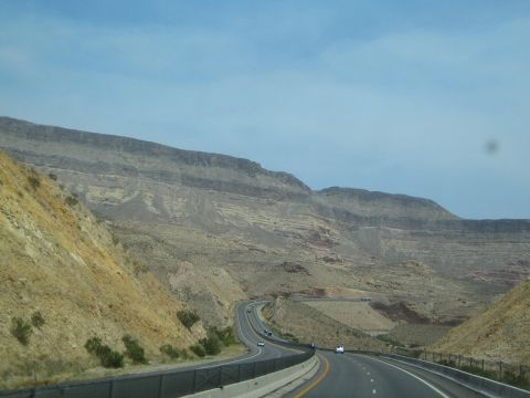 1990 Ford Bronco - desert highway curves through a valley beneath long horizontally layered mesa cliffs.