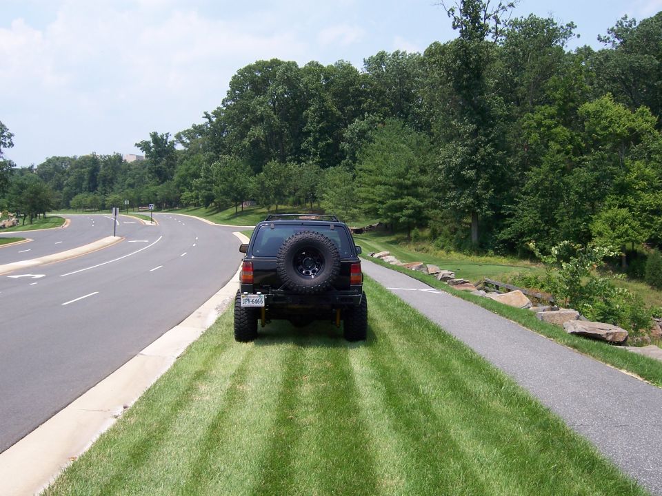 Black 1996 Jeep Grand Cherokee parked on grass next to a road, spare tire mounted on the rear door