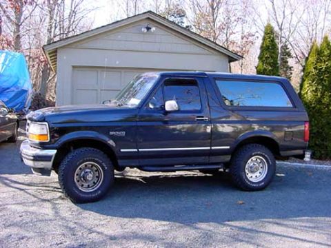 1996 Ford Bronco - A dark blue 1996 Ford Bronco is parked outside a garage on a sunny day.