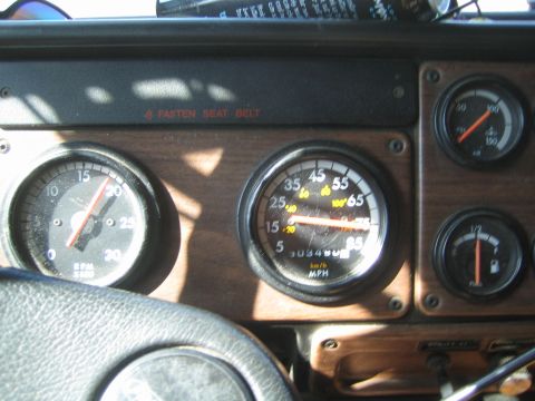 1990 Ford Bronco - truck's wood-grain instrument panel displays a tachometer, MPH speedometer and auxiliary gauges with a Fasten Seat Belt indicator.