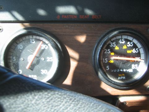 1990 Ford Bronco - Sunlight falls across a truck's wood-trim dash showing the tachometer and MPH speedometer gauges.
