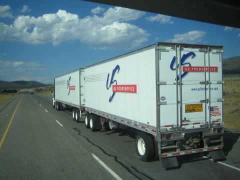 1990 Ford Bronco - white U.S. Foodservice semi pulling double trailers drives a highway beneath bright cumulus clouds.