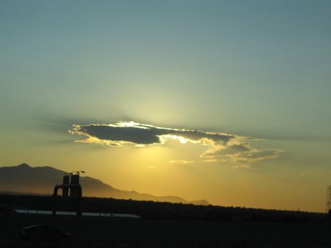 1990 Ford Bronco - sun sets behind a backlit cloud over a mountain silhouette with a dark roadside structure in foreground.