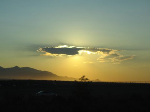 1990 Ford Bronco - golden sunset glows behind a dramatic cloud over mountains with a parked car silhouetted below.