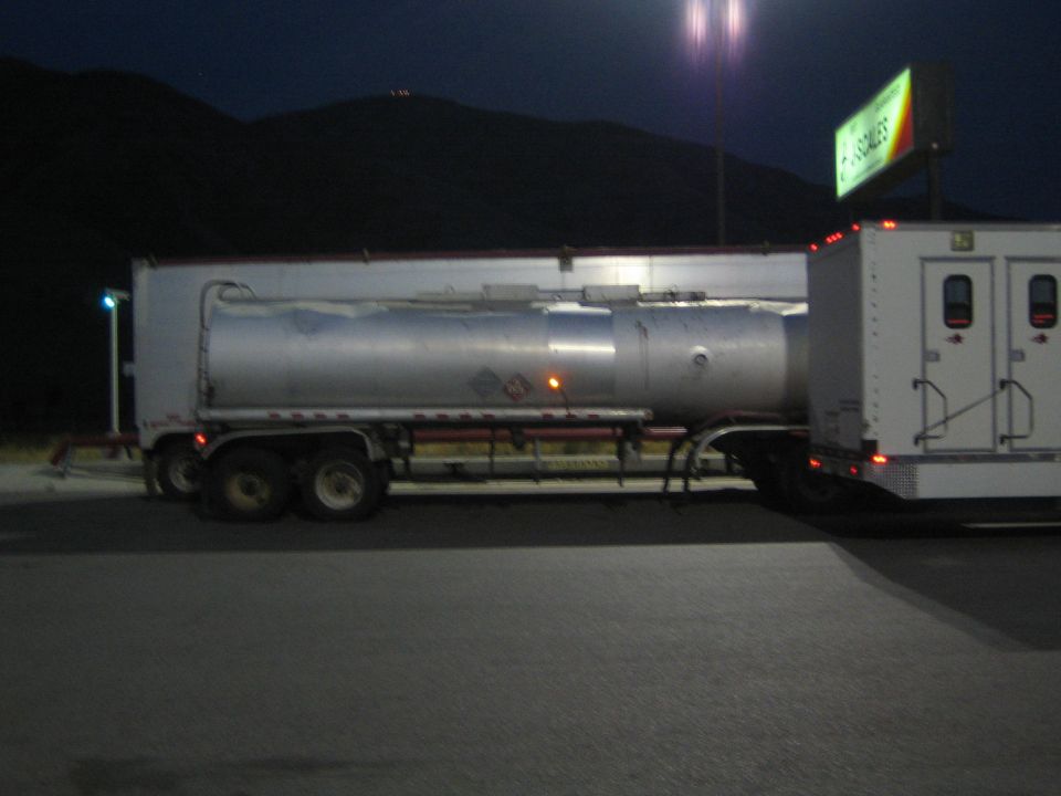 Side view of a silver tanker trailer parked at night under lights
