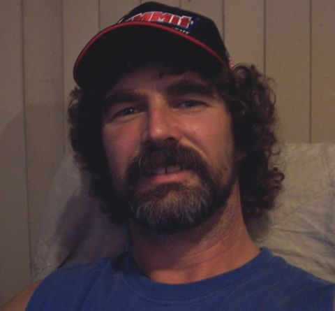 1990 Ford Bronco - A man with a beard and curly hair is wearing a baseball cap and a blue shirt.